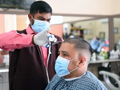 Seorang barber yang mengenakan masker memangkas rambut pelanggan di pasar Al-Mubarakiya di Kuwait City, Kuwait (18/8/2020). Kuwait mulai Selasa (18/8) memasuki tahap keempat dari rencana lima tahapnya untuk kembali ke kehidupan normal. (Xinhua/Ghazy Qaffaf)