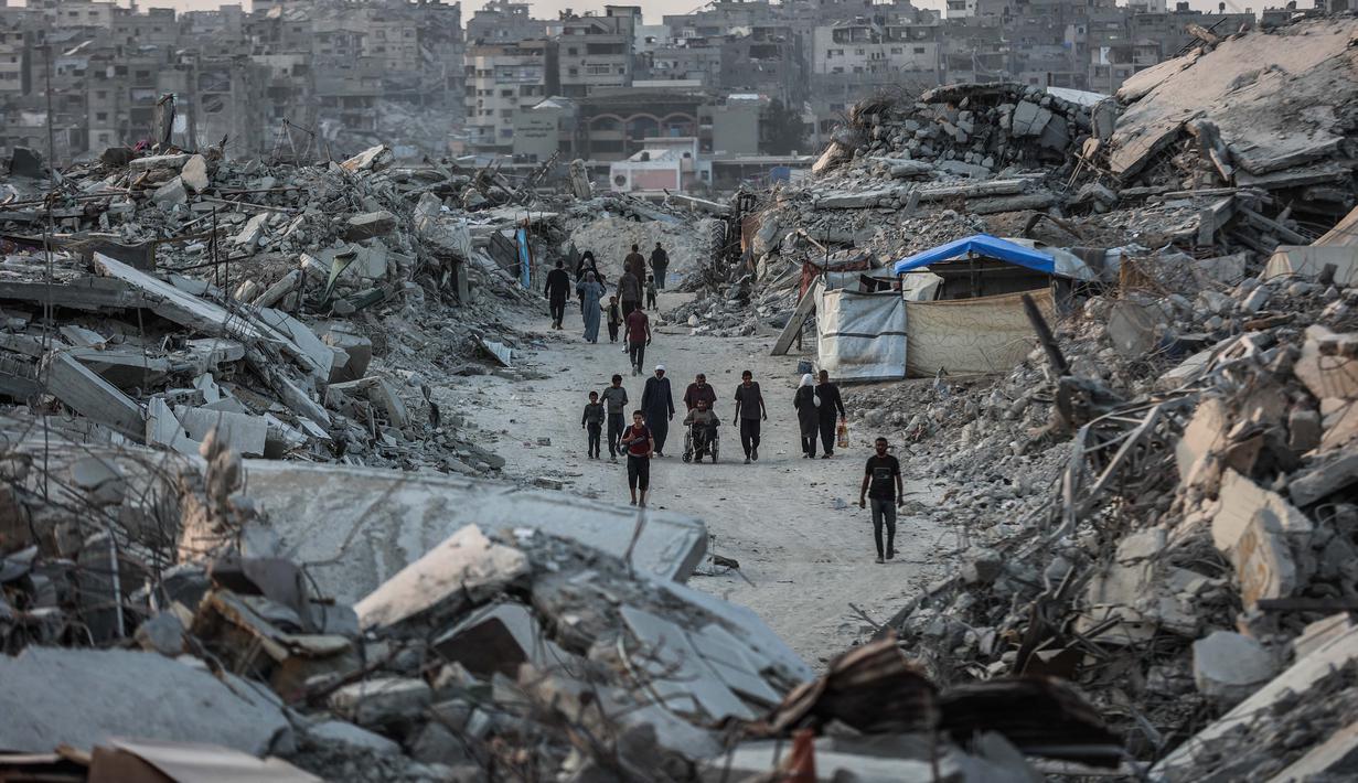 Akses bantuan, terutama ke wilayah utara Gaza, masih sangat terbatas, dan banyak permintaan bantuan ditolak oleh pihak berwenang Israel. Tampak dalam foto, warga Palestina berjalan di antara puing-puing bangunan yang hancur di Jabalia, di bagian utara Jalur Gaza, pada Jumat 7 November 2025. (Omar AL-QATTAA/AFP)