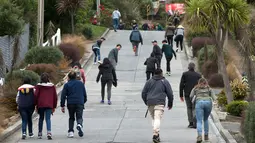 Wisatawan berjalan menyusuri jalanan paling curam di dunia, Baldwin Street, di kota Dunedin, Selandia Baru, 26 Agustus 2017. Jalanan sepanjang 350 meter itu memiliki kemiringan yang ekstrem, yakni 1:2.86 dengan gradien 35 persen. (AP Photo/Mark Baker)