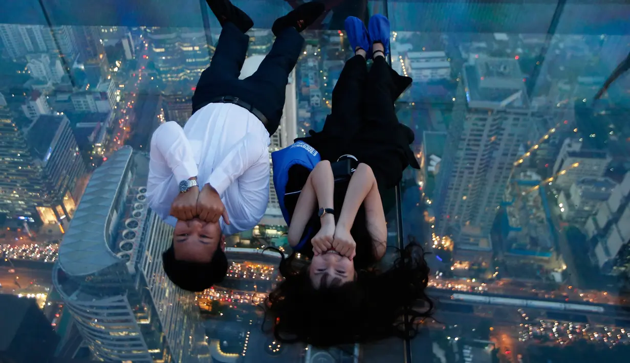 Sepasang wisatawan berpose di dek kaca gedung King Power Mahanakhon, Bangkok, Thailand, Rabu (21/11). Gedung King Power Mahanakhon memiliki tinggi 314 meter atau sekitar 10.249 kaki. (AP Photo/Sakchai Lalit)