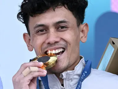 Atlet panjat tebing Indonesia, Veddriq Leonardo menggigit medali emas saat di atas podium cabang olahraga panjat tebing nomor speed Olimpiade Paris 2024 di Le Bourget Sport Climbing Venue, Paris, Prancis, Kamis (08/08/2024). (AFP/Jonathan Nackstrand)