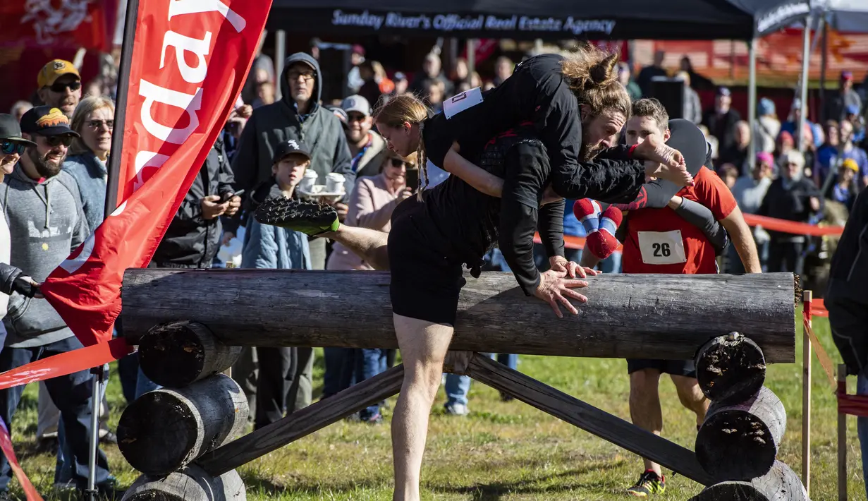 John Lund menggendong Karen May melewati rintangan selama North American Wife Carrying Championship di Sunday River Resort di Newry, Maine, pada 8 Oktober 2022. Kejuaraan ini seakan menguji pengorbanan para suami yang rela menggendong istrinya dengan melewati berbagai rintangan. (Joseph Prezioso / AFP)