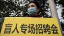 Seorang wanita memegang poster bertulisan "job fair for blind people" saat dia mengenakan masker pelindung untuk menghindari polusi udara buruk di Beijing (22/10). (AFP Photo/Nicolas Asfaouri)