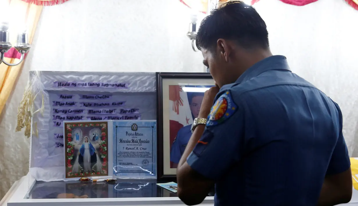 Seorang petugas kepolisian berdoa di depan jasad Rancel Cruz yang mati di tembak pecandu narkoba di Manila, Filipina, (19/10). Langkah tegas pemerintah Filipina membuat para pengguna narkoba membalas menembak petugas. (REUTERS/Erik De Castro)
