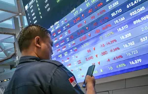 Seorang pria melihat ponselnya di depan layar yang menampilkan Indeks Harga Saham Gabungan (IHSG), yang anjlok signifikan selama pembukaan pasar, di gedung Bursa Efek Indonesia di Jakarta pada Rabu 13 Mei 2026. (BAY ISMOYO/AFP)