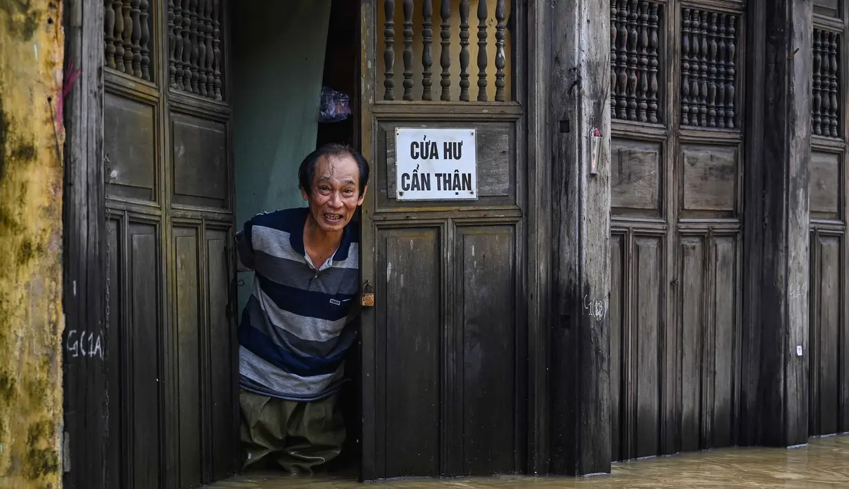 Seorang pria berdiri di tengah banjir di pintu masuk sebuah toko setelah hujan deras di Hoi An, Vietnam, Kamis 30 Oktober 2025. Laporan pemerintah setempat, pada Rabu (29/10/2025), enam dari korban tewas berasal dari Da Nang dan Hoi An, dua kawasan wisata populer di negara itu. (NHAC NGUYEN/AFP)