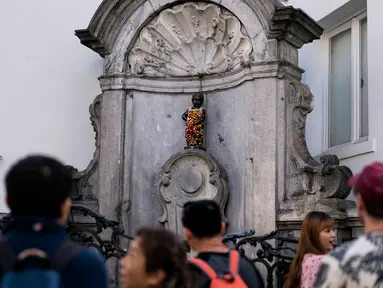 Wisatawan berfoto dekat patung 'Manneken Pis' dalam balutan baju bermotif bunga di ibu kota Belgia, Brussels, Senin (12/8/2019). Patung anak laki-laki yang sedang buang air kecil ini menjadi salah satu daya tarik uta di kota cantik tersebut. (Photo by Kenzo TRIBOUILLARD / AFP)