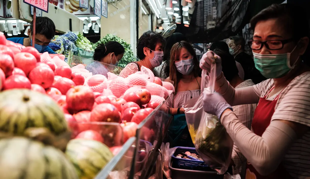 Pedagang mengenakan masker melayani pelanggan di toko buah dan sayuran di Hong Kong (21/4/2020). Hong Kong melaporkan penurunan kasus infeksi harian Covid-19, tetapi pemerintah kota mengatakan mereka tidak mengambil risiko apa pun. (AFP/Anthony Wallace)