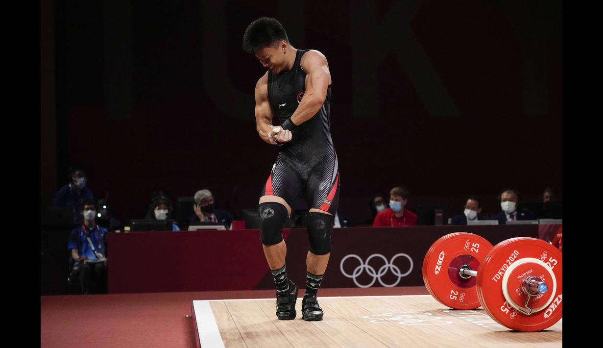 Atlet angkat besi asal Indonesia Rahmat Erwin Abdullah menunjukkan ototnya kepada penonton usai berhasil meraih medali perunggu dari cabang angkat besi 73kg putra Olimpiade Tokyo 2020, Rabu (28/7/2021). (Foto: AP/Luca Bruno)