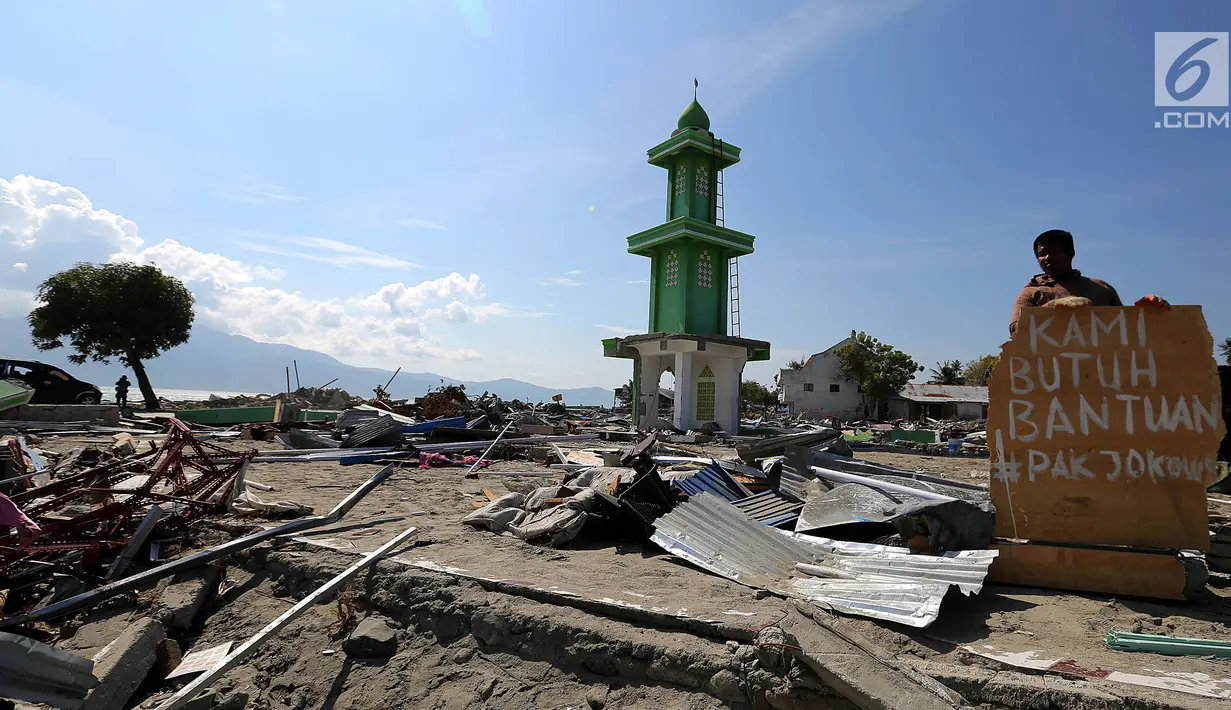 Warga membawa papan bertuliskan Kami Butuh Bantuan Pak Jokowi di atas reruntuhan puing pasca gempa bumi dan tsunami di Jalan Trans Sulawesi, Palu, Sulawesi Tengah, Kamis (4/10). (Liputan6.com/Fery Pradolo)