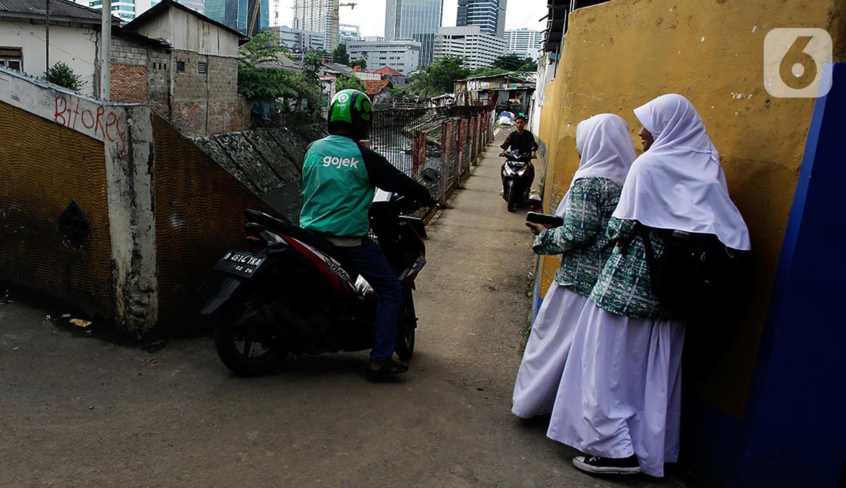 Pengendara sepeda motor melintasi jalur alternatif saat anak sekolah berjalan di belakang Kompleks Patra Jasa, Jakarta Selatan, Rabu (1/3/2023). Jalur alternatif seperti gang, jalan kecil, maupun jalan tembusan menjadi pilihan bagi pengendara sepeda motor untuk menghindari kemacetan di jalan-jalan protokol Ibu Kota. (Liputan6.com/Johan Tallo)
