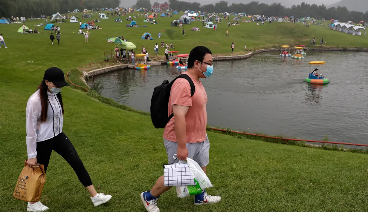 Sepasang suami istri melewati orang-orang yang berkemah di gunung yang indah di Yanqing, pinggiran Beijing, 30 Agustus 2020. China memiliki lebih dari 200 orang yang dirawat di RS karena COVID-19, dengan lebih dari 300 lainnya diisolasi usai dites positif terkena virus tanpa gejala. (AP/Andy Wong)