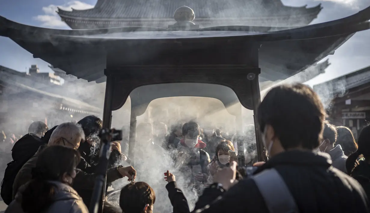 Orang-orang berdoa di sekitar pembakar dupa di kuil Sensoji menjelang liburan Tahun Baru di Tokyo pada 30 Desember 2022. Pada malam tahun baru, joya no kane atau lonceng malam tahun baru akan berdentang nyaring dari kuil ini. Lonceng tersebut menandakan bahwa pada saat itu hari dan tahun telah berganti menjadi 1 Januari. (AFP/Yuichi Yamazaki)