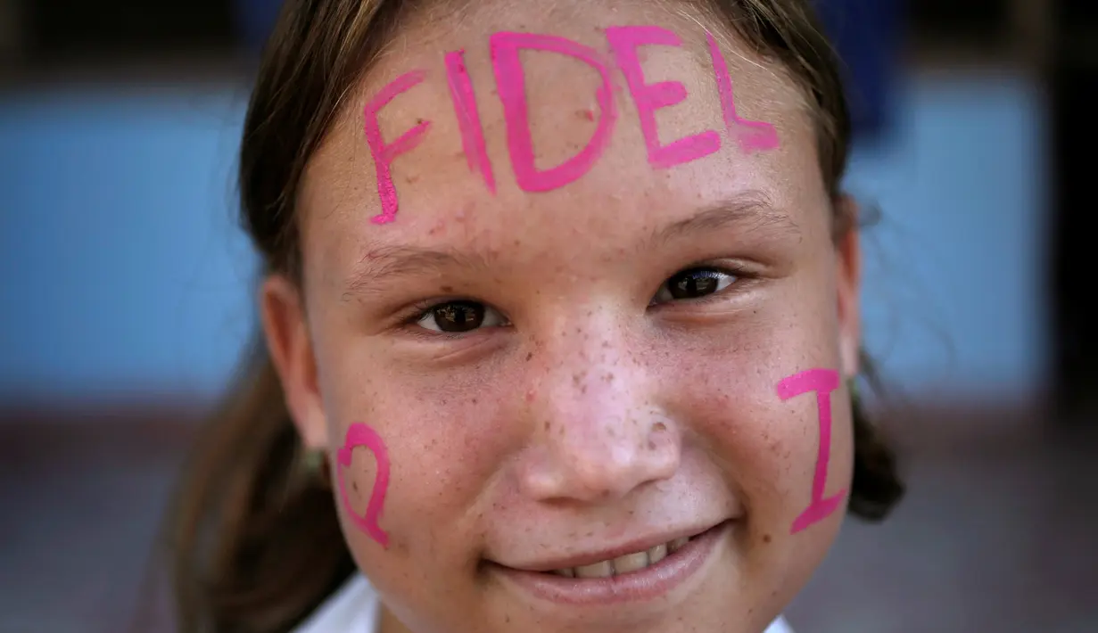 Seorang anak tersenyum dengan tulisan Fidel di wajahnya saat menunggu mobil yang membawa abu mantan pemimpin Revolusi Kuba, Fidel Castro, lewat di Bayamo, Kuba (3/11). (Reuters/Enrique De La Osa)