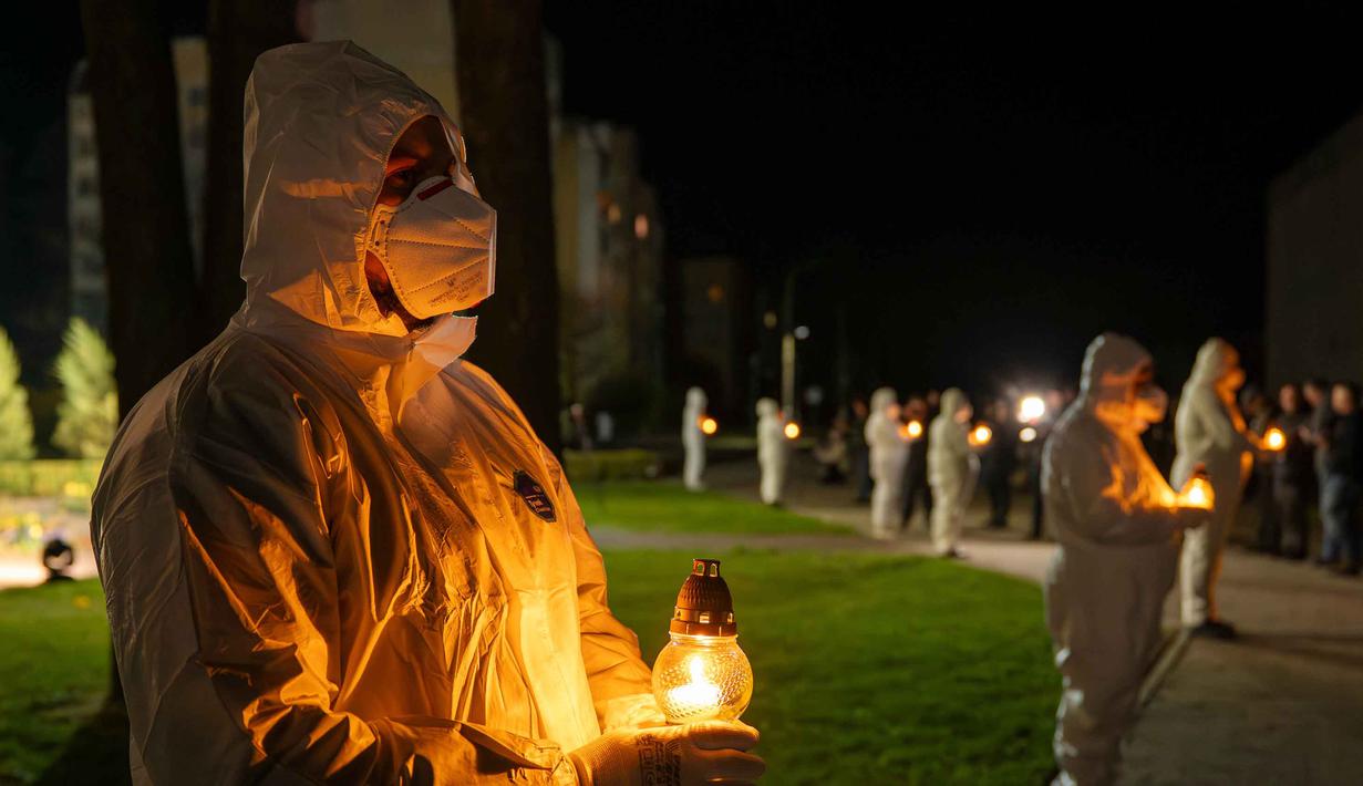 Orang-orang yang mengenakan pakaian pelindung putih memegang lilin selama upacara peringatan yang didedikasikan untuk petugas pemadam kebakaran dan pekerja yang meninggal setelah bencana nuklir Chernobyl, menjelang peringatan 40 tahunnya di Slavutych, Ukraina, Sabtu, 25 April 2026. (AP Photo/Dan Bashakov)