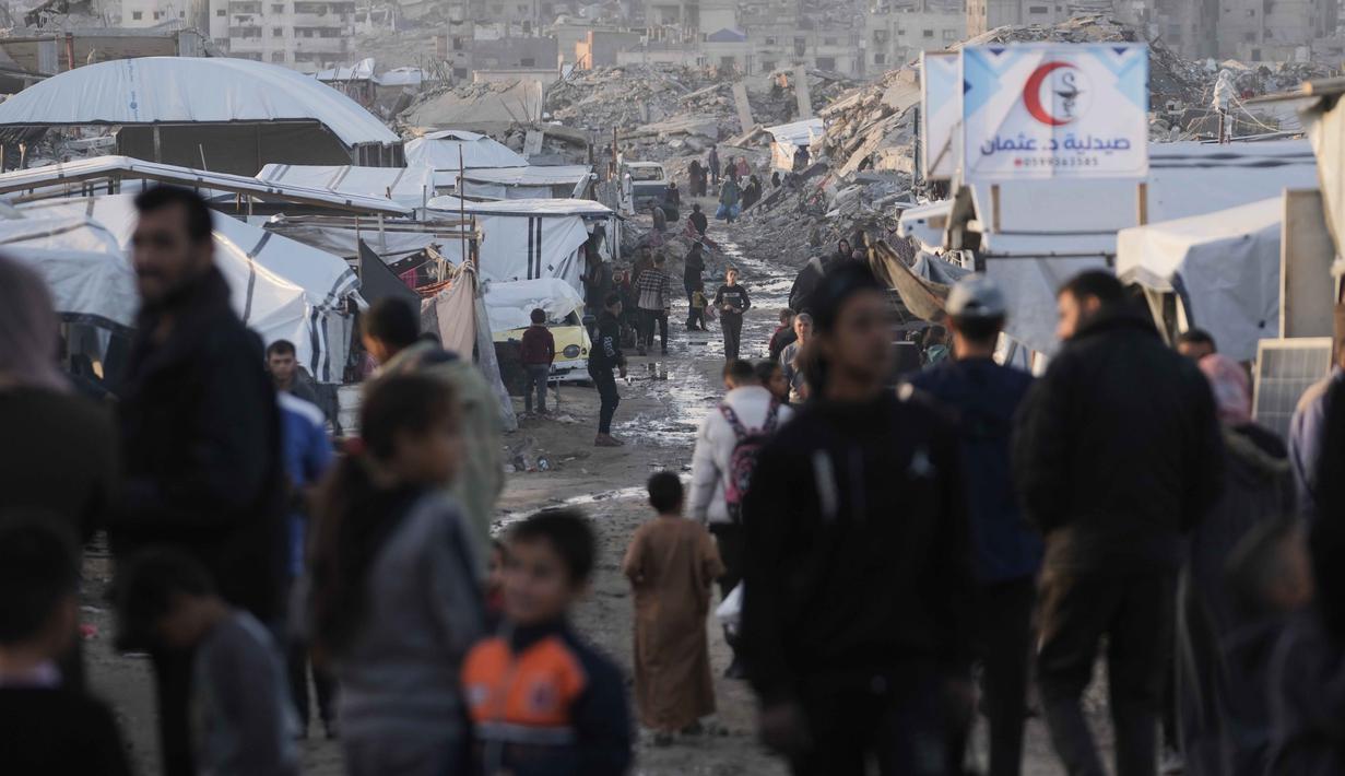 Upaya pemulihan yang signifikan belum dapat dilakukan secara efektif di tengah situasi keamanan yang masih bergejolak. Tampak dalam foto, pengungsi Palestina berjalan melalui jalan berlumpur di antara tenda-tenda yang didirikan di antara bangunan-bangunan yang hancur di Jabalia, di bagian utara Jalur Gaza, Minggu 7 Desember 2025. (AP Photo/Jehad Alshrafi)