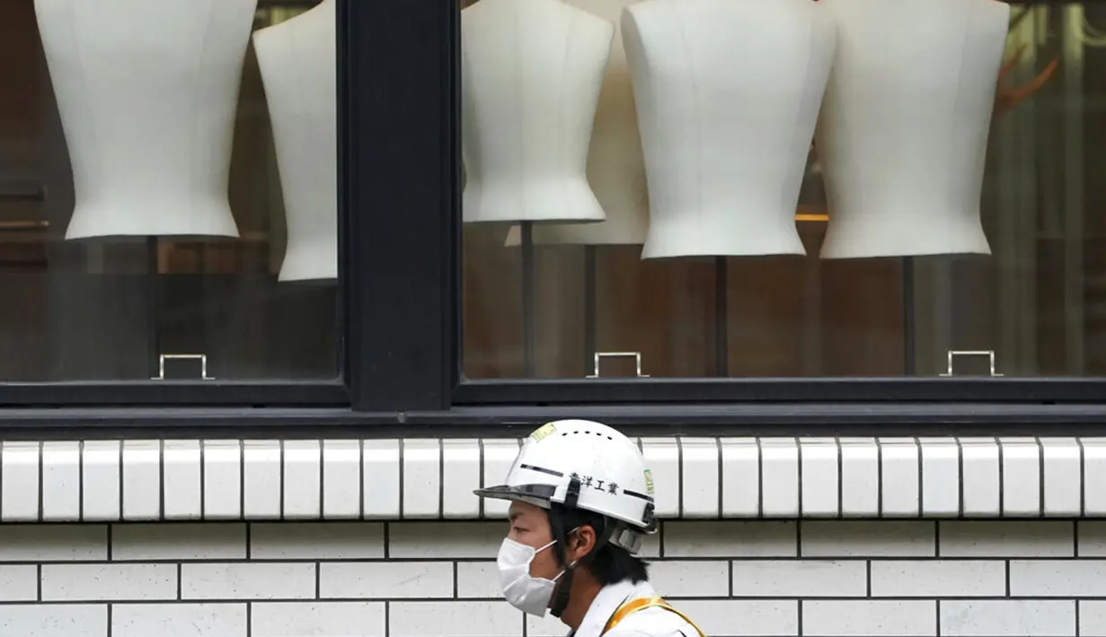 Seorang pekerja konstruksi yang mengenakan masker untuk membantu mengekang COVID-19 berjalan melewati sebuah toko pakaian di Tokyo, Jepang, Senin (2/11/2020). Tokyo mengonfirmasi lebih dari 80 kasus baru COVID-19 pada 2 Oktober 2020. (AP Photo/Eugene Hoshiko)