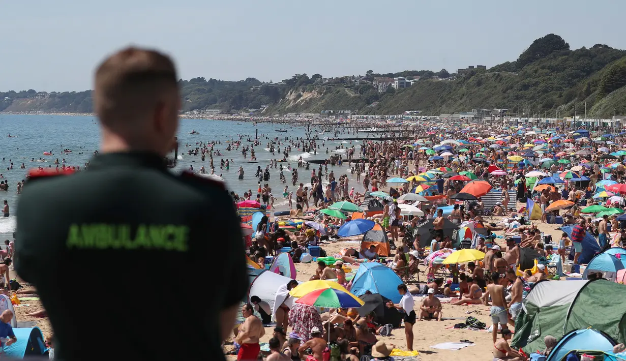 Petugas layanan ambulans memandangi kerumunan pengunjung yang berkumpul di pantai di Bournemouth, Kamis (25/6/2020). Pantai tersebut diserbu warga Inggris, setelah masa pelonggaran pembatasan sosial akibat covid-19 dan pembatasan perjalanan Eropa. (Andrew Matthews/PA via AP)