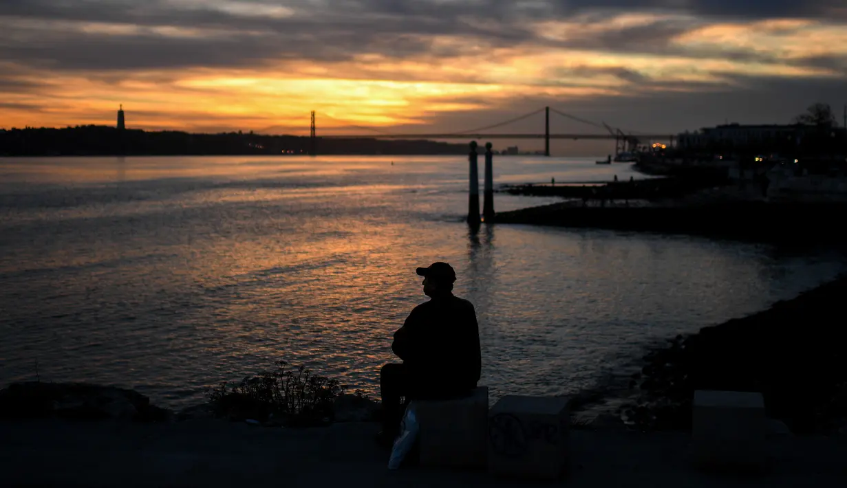 Seorang pria menyaksikan matahari terbenam di Cais das Colunas di Lisbon (17/12). (AFP Photo/Patricia De Melo Moreira)