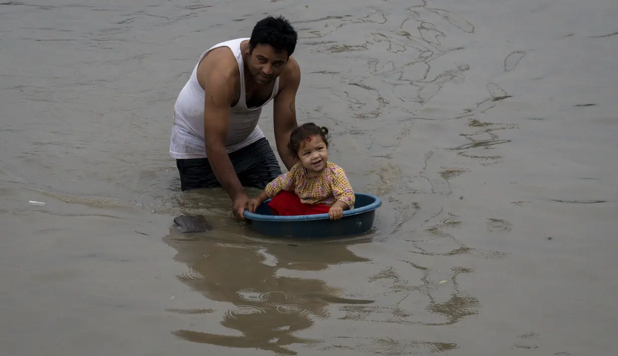 Seorang pria meletakkan anaknya di wadah plastik untuk bermain di air banjir sungai Bagmati setelah hujan deras di Kathmandu, Nepal, Selasa (8/8/2023). (AP Photo/Niranjan Shrestha)