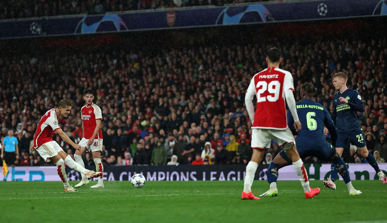 Pemain Arsenal, Martin Odegaard mencetak gol dari luar kotak penalti pada laga Grup B Liga Champions 2023/2024 melawan PSV Eindhoven di Emirates Stadium, London, Kamis (21/09/2023) dini hari WIB. Bola tendangan kaki kiri Odegaard mengarah ke pojok kanan bawah kiper PSV, Walter Daniel Benitez. (AFP/Adrian Dennis)