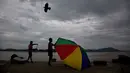 Seorang penjual ikan memegangi payungnya yang tertiup angin di tepi sungai Brahmaputra, India, Selasa (30/5). Beberapa negara bagian di India timur laut mengalami hujan deras sebagai efek topan Mora yang melanda selatan Bangladesh. (AP Photo/Anupam Nath)