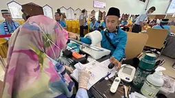 Setibanya di lokasi, para jemaah langsung menjalani proses pemeriksaan kesehatan, penyelesaian administrasi, serta penguatan manasik haji dan sosialisasi kesehatan. Tampak dalam foto, petugas memeriksa kesehatan calon haji setibanya di Asrama Haji Pondok Gede, Jakarta, Selasa (21/4/2026). (merdeka.com/Arie Basuki)