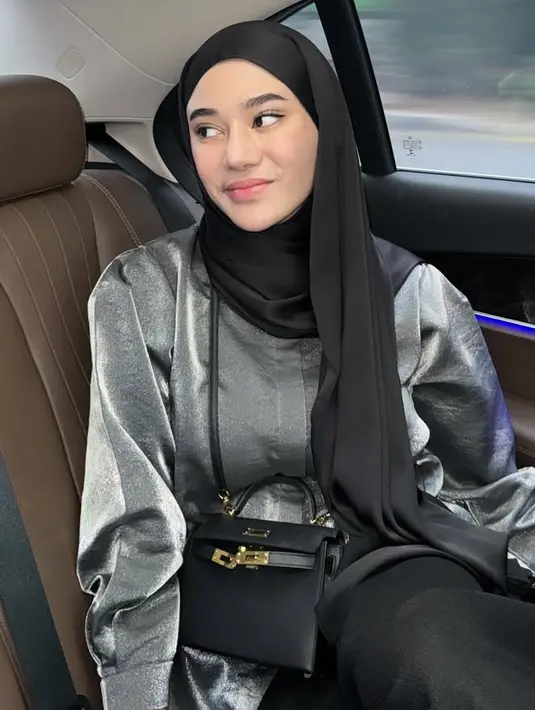 Kerudung hitam panjang model pashmina juga dikenakan olehnya. Dipadukan atasan kemeja loose silver serta rok dan tas Hermes hitam. [@clarashintareal]