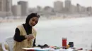 Lokakarya Bernapas dan Melukis menjadikan seni dan budaya untuk membangun kembali kepercayaan diri dan harapan. Tampak dalam foto, seorang perempuan muda melukis di pelabuhan Kota Gaza pada Kamis 12 Februari 2026. (Omar AL-QATTAA/AFP)