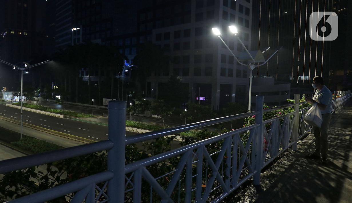 Warga melihat suasana jalan lengang kawasan Sudirman, Jakarta, Rabu (12/5/2021) malam. Polda Metro Jaya memberlakukan crowd free night untuk mencegah kerumunan takbir keliling di malam Idul Fitri 1442 yang berlaku mulai pukul 22:00 malam ini. (Liputan6.com/Herman Zakharia)