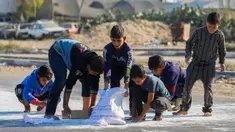Anak laki-laki Palestina mengais tepung dari jalan setelah sebuah tas jatuh dari truk bantuan yang melaju di jalan Salaheddin di Deir el-Balah di Jalur Gaza tengah pada 5 November 2024. (Eyad BABA/AFP)