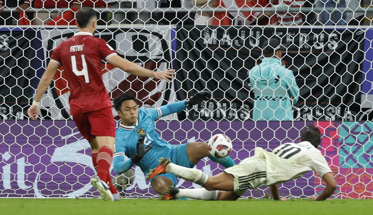 Kiper Timnas Indonesia, Ernando Ari Sutaryadi (tengah) berhasil memblok sundulan striker Timnas Irak, Mohanad Ali pada laga pertama Grup D Piala Asia 2023 Qatar di Ahmad bin Ali Stadium, Al-Rayyan, Doha, Senin (15/1/2024). (AFP/Karim Jaafar)