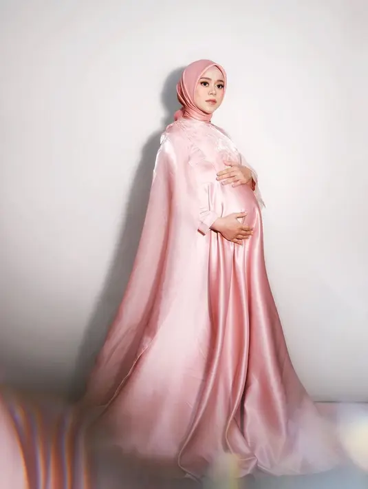 Maternity shoot yang dilakukan Lesty Kejora juga sempat mencuri perhatian banyak orang. Seperti tampilannya di sini yang memakai dress dan hijab satin bernuansa merah muda. Dress polos ini diberi detail bahan organza di bagian dada dan memanjang menjadi cape. Foto: Instagram.