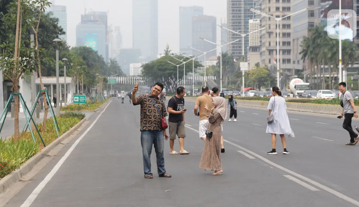 Warga memanfaatkan kondisi lengang sebagian ruas jalan Jenderal Sudirman untuk berfoto, Jakarta, Minggu (27/10/2019). Sebagian ruas Jalan Jenderal Sudirman dialihkan akibat  berlangsungnya Karnaval Kendaraan Listrik yang bertajuk Jakarta Langit Biru. (Liputan6.com/Helmi Fithriansyah)