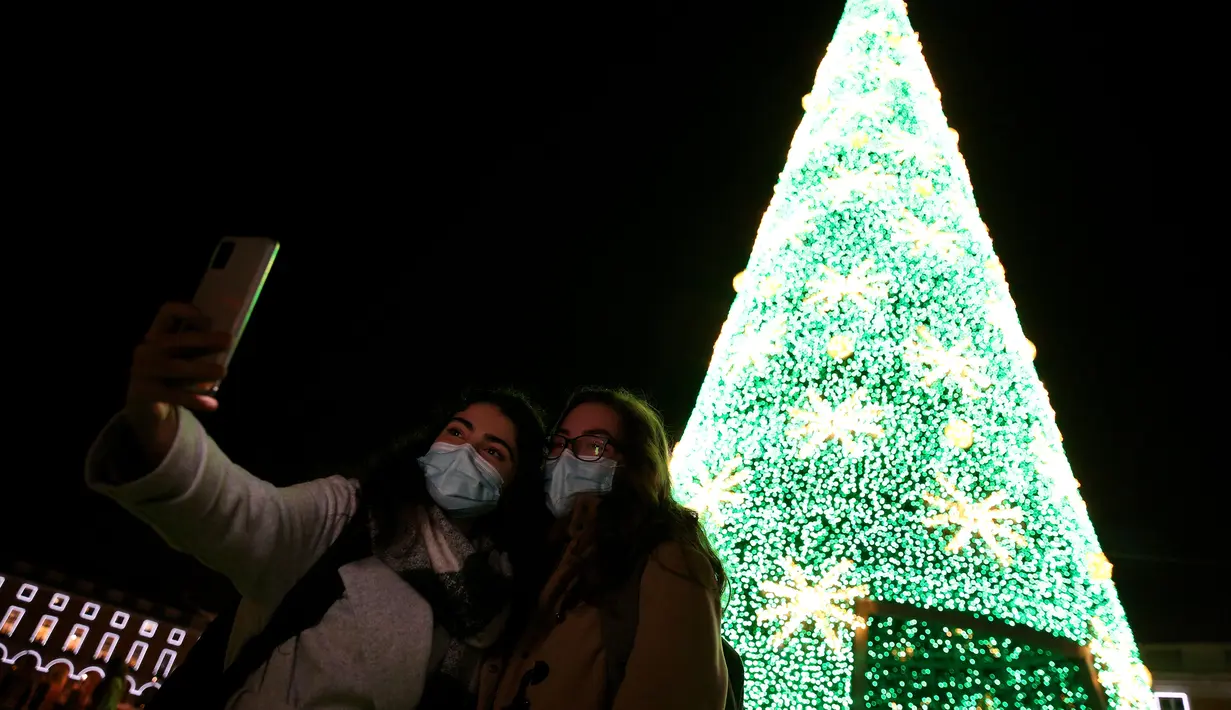 Sejumlah warga yang mengenakan masker berpose untuk difoto di bawah lampu-lampu Natal dan Tahun Baru pada masa pandemi COVID-19 di Kota Lisbon, Portugal, 17 Desember 2020. Warga Portugal tidak diizinkan meninggalkan rumah antara pukul 13.00 - 05.00 mulai 1 Januari - 3 Januari. (Xinhua/Pedro Fiuza)