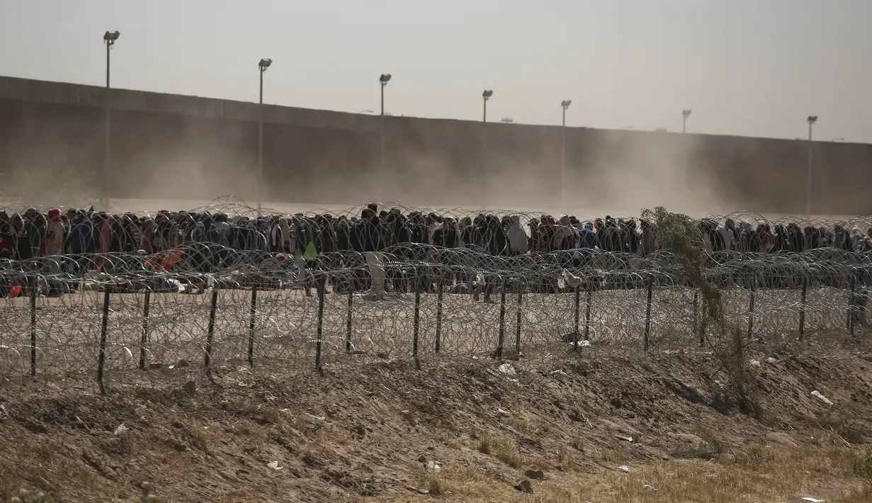 Migran berbaris antara penghalang kawat berduri dan pagar perbatasan di perbatasan AS-Meksiko, seperti yang terlihat dari Ciudad Juarez, Meksiko, Selasa (9/5/2023). (AP Photo/Christian Chavez)