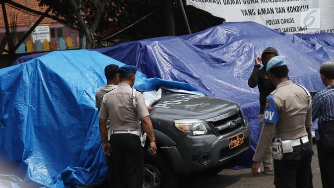 Petugas melihat melihat kondisi mobil yang dirusak di Polsek Ciracas, Jakarta, Rabu (12/12). Sekelompok orang tak dikenal merusak sekitar 17 mobil dinas. (Liputan6.com/Herman Zakharia)