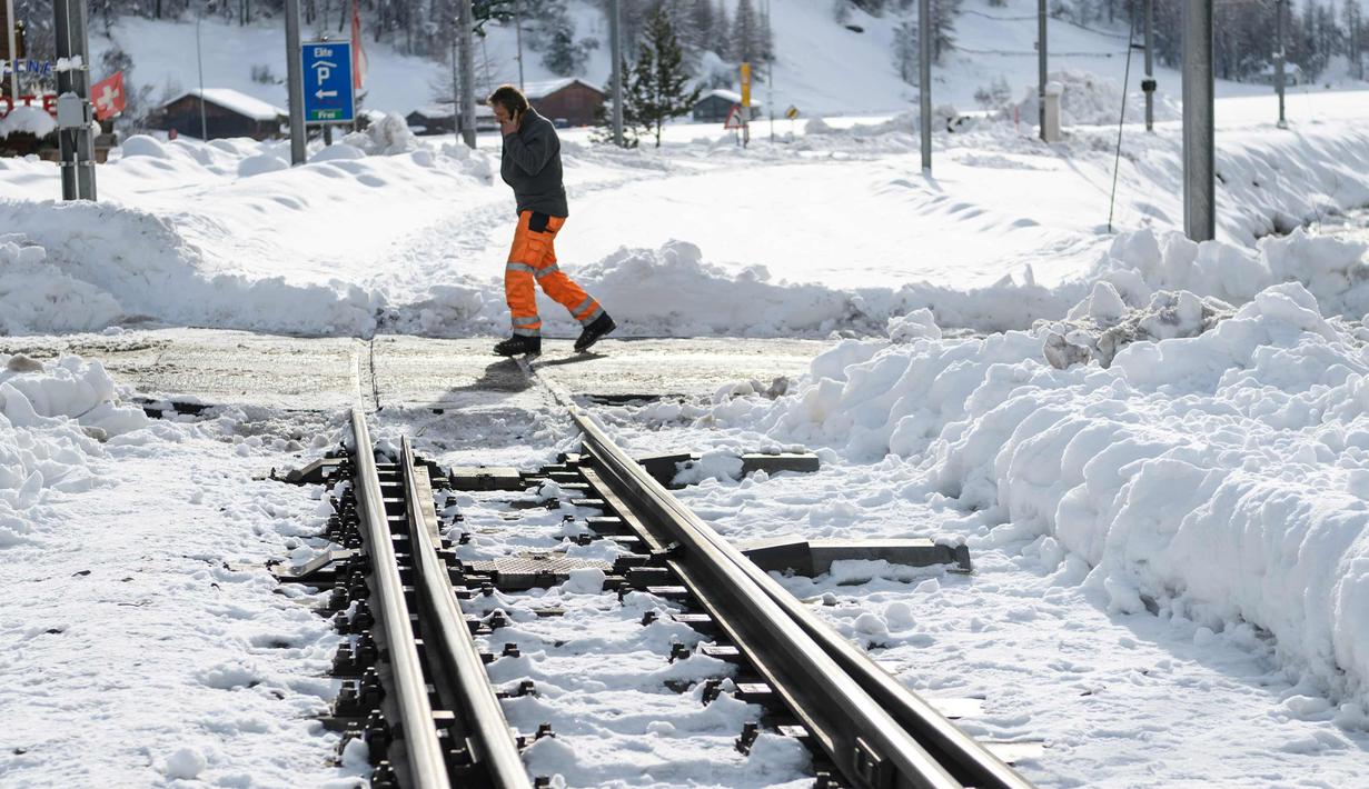 Seorang petugas memeriksa kondisi rel kereta api yang tertutup salju tebal di salah satu resor ski paling populer di Swiss (10/1). Sekitar 13.000 wisatawan terjebak akibat bencana tersebut. (AFP Photo/Fabrice Coffrini)