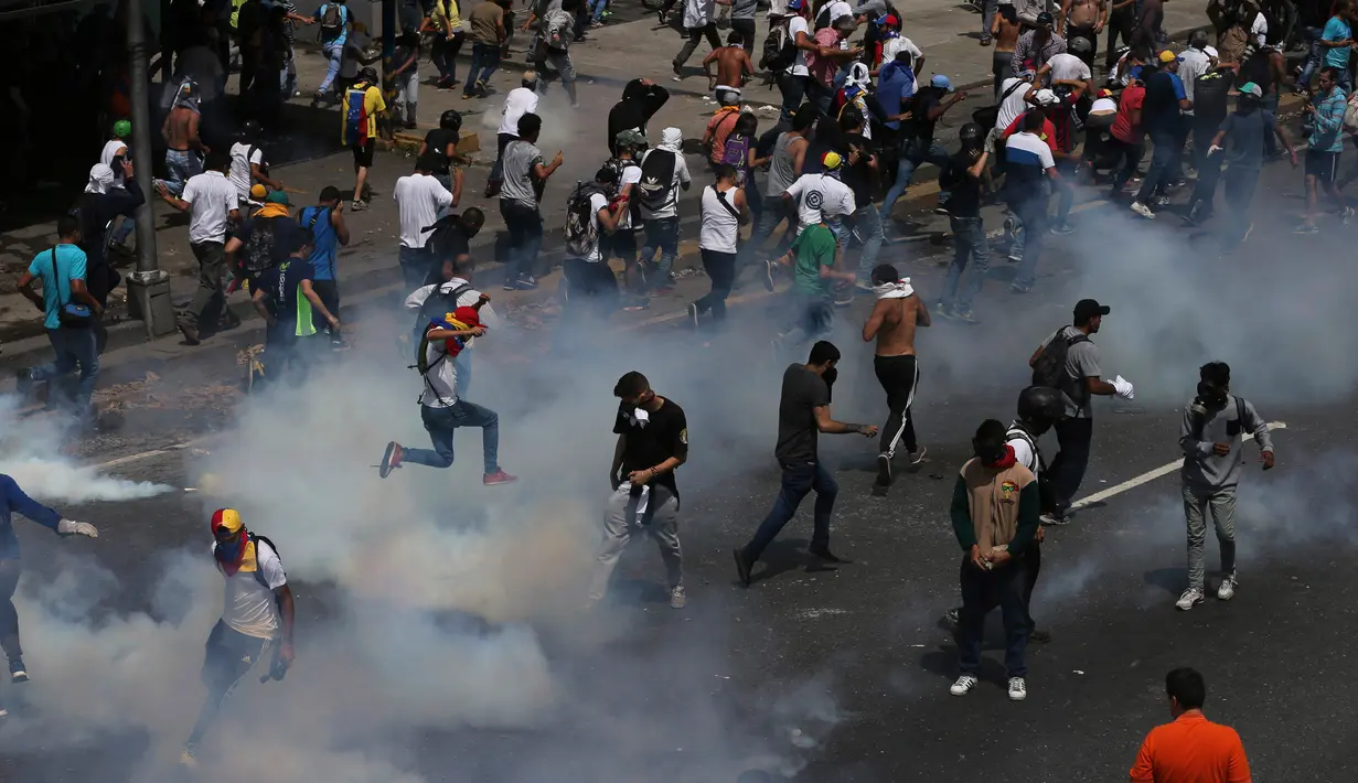 Para demonstran menghindari tembakan gas air mata saat bentrokan terjadi di Caracas, Venezuela, (6/4). Lemparan batu, tembakan gas air mata hingga meriam air warnai bentrokan demonstran anti-Maduro dan polisi di Venezuela. (AP Photo / Fernando Llano)
