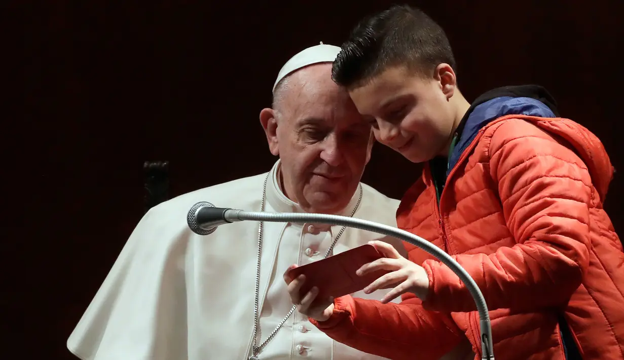 Seorang anak laki-laki dan Paus Fransiskus mengamati ponsel untuk melihat hasil foto selfie mereka dalam kunjungannya ke St Mary Josefa di Roma, Italia, Minggu (19/2). (AP Photo/Alessandra Tarantino)