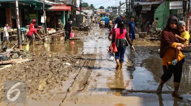 Warga melintas di sepanjang jalan yang dipenuhi lumpur di komplek Pondok Gede Permai Jatiasih, Bekasi, Jumat (22/04). Banjir yang telah merendam ratusan rumah warga mengakibatkan air lumpur mengendap. (Liputan6.com/Fery Pradolo)