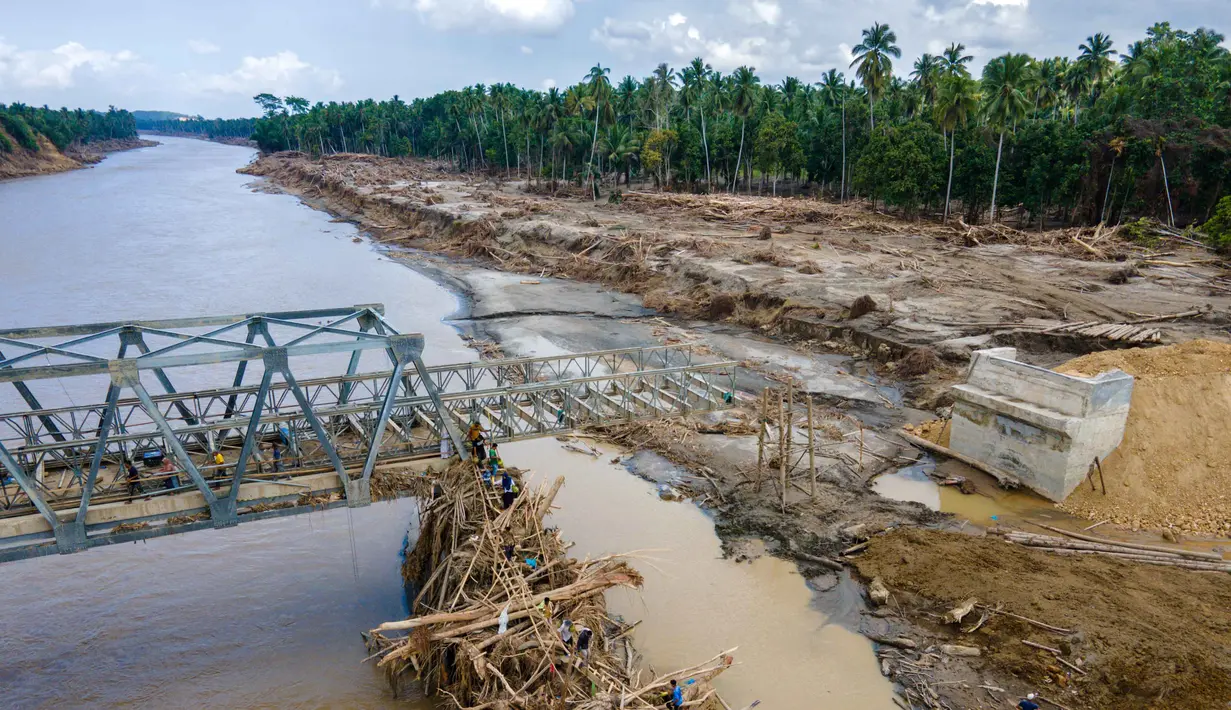 Struktur jembatan baja tersebut ditargetkan menjadi penghubung sementara agar mobilitas masyarakat dan distribusi logistik ke wilayah terdampak dapat kembali berjalan. Tampak foto udara menunjukkan warga memanjat puing-puing untuk menyeberangi sungai di jembatan yang baru dibangun yang menghubungkan Aceh dan Provinsi Sumatera Utara setelah hancur akibat banjir bandang di Sungai Peusangan di Distrik Bireuen, Provinsi Aceh, pada Selasa 9 Desember 2025. (CHAIDEER MAHYUDDIN/AFP)