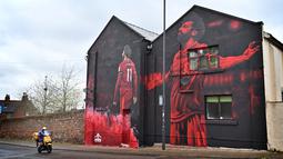 Pengendara skuter melewati mural seniman John Culshaw yang menggambarkan pesepak bola Mesir Mohamed Salah di fasad bangunan dekat Stadion Anfield, Liverpool, Rabu (30/3/2022). Salah tidak diragukan lagi, adalah salah satu pemain terhebat yang pernah mengenakan seragam Liverpool. (Paul ELLIS / AFP)