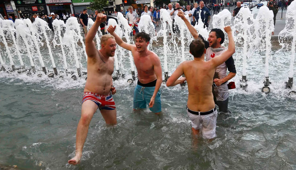 Sejumlah suporter Inggris bernyanyi merayakan kemenangan Timnas Inggris di kolam air mancur yang berada di tengah Kota Lille, Prancis (16/6). Aksi suporter Inggris menjadi tontonan warga yang melintasi kawasan tersebut. (REUTERS / Wolfgang Rattay)
