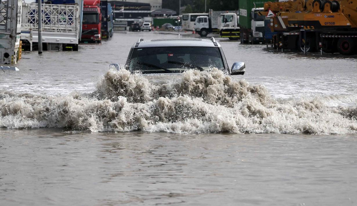 Pengendara mobil terpaksa menerobos banjir sementara air merendam hampir seluruh bagian rodanya. Tampak dalam foto, sebuah kendaraan melaju melewati genangan air setelah hujan lebat, di Dubai, Uni Emirat Arab (UEA) pada Jumat 19 Desember 2025. (FADEL SENNA/AFP)