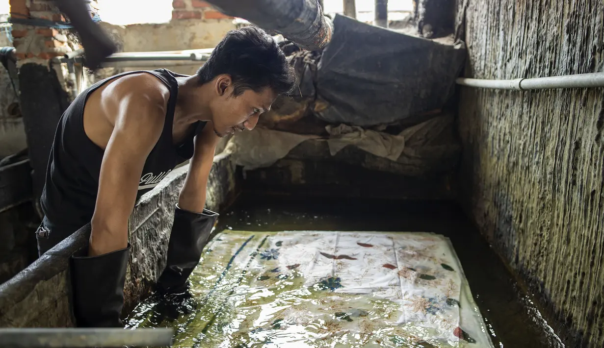 Seorang pekerja merendam batik di pabrik "batik" kain tradisional Indonesia di Sidoarjo, Jawa Timur (12/11/2019). UNESCO menetapkan batik sebagai karya agung lisan dan warisan budaya takbenda kemanusiaan. (AFP Photo/Juni Kriswanto)