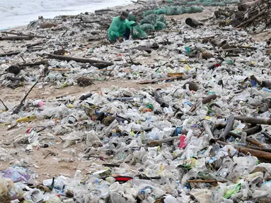 Seorang pria mengumpulkan plastik dan sampah lainnya yang terdampar di pantai Kedonganan, Kabupaten Badung, Bali, pada Jumat 27 Desember 2024. (SONNY TUMBELAKA/AFP)