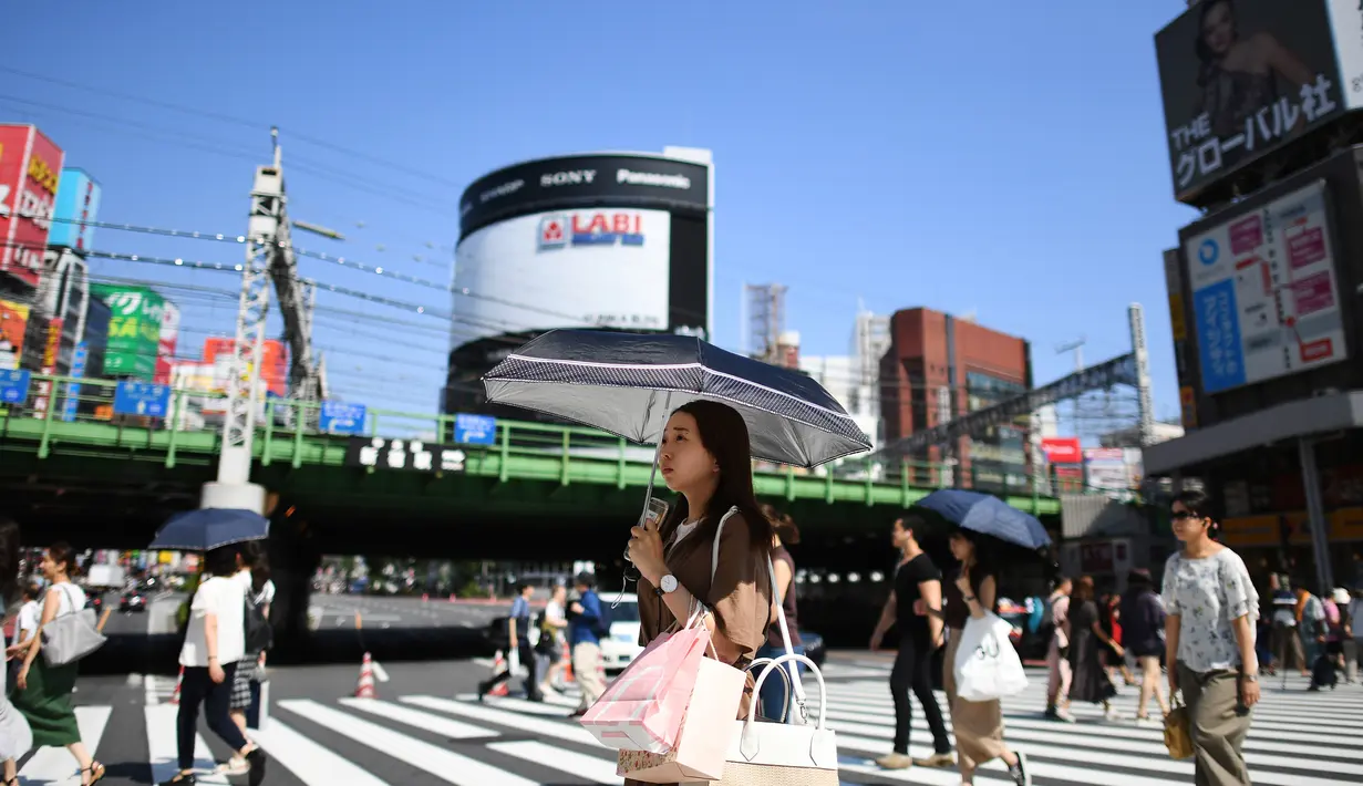 Seorang wanita menggunakan payung untuk melindungi dirinya dari sinar matahari selama gelombang panas saat melintasi jalan di distrik Shinjuku Tokyo, Minggu (4/8/2019). Setelah menyerang beberapa wilayah di Eropa, suhu tinggi juga terjadi di Jepang. (Charly TRIBALLEAU / AFP)