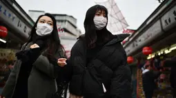 Dua wanita memakai masker berjalan di sepanjang jalan dekat kuil Sensoji di daerah Taito Tokyo (27/1/2020). Masker dipilih sebagai salah satu tindak pencegahan sederhana dari virus dengan karakteristik mirip SARS tersebut. (AFP Photo/Charly Triballeau)
