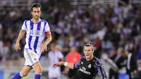 Penyerang Real Madrid, Gareth Bale (tengah) berjibaku kontra bek Real Sociedad, Joseba Zaldua (kanan), pada laga pembuka La Liga 2016-2017, di Stadion Anoeta, Senin (22/8/2016) dini hari WIB. Bale mencetak dua gol.  (AFP/Ander Gillenea)